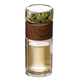 Glass tumbler with wooden sleeve containing green leaves on a white background