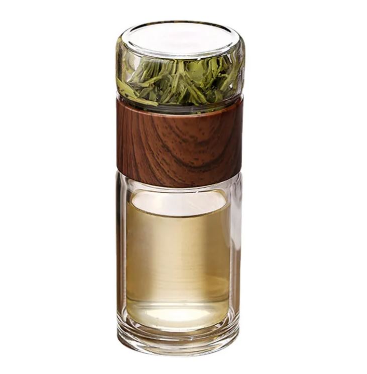 Glass tumbler with wooden sleeve containing green leaves on a white background