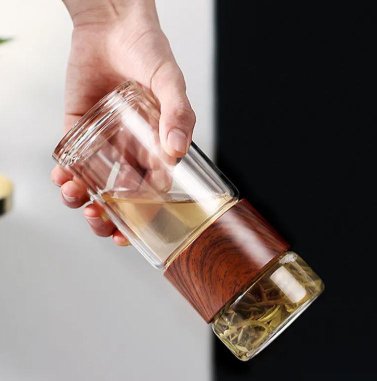 Glass tea infuser with wooden handle held by a hand