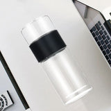 Clear glass bottle with black lid on a white surface next to a laptop