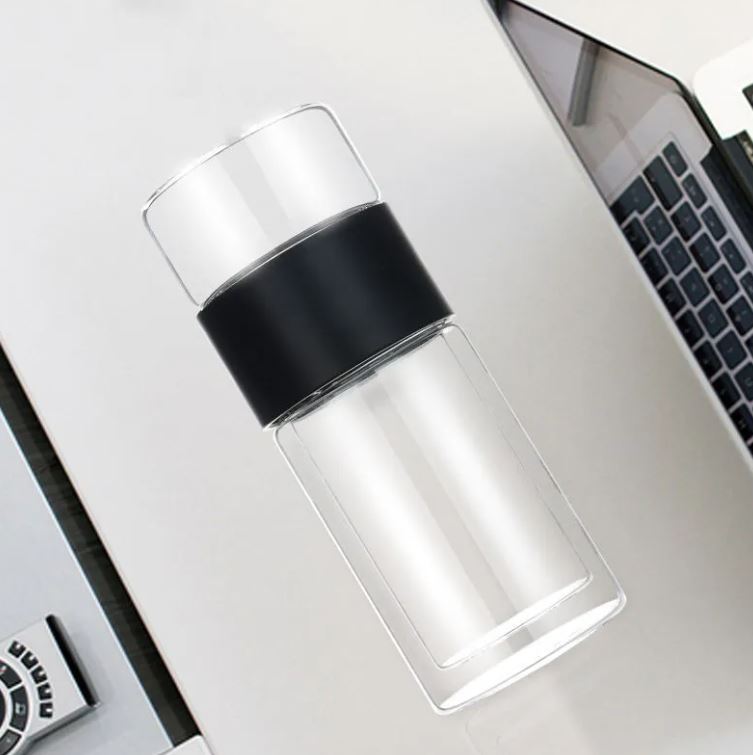 Clear glass bottle with black lid on a white surface next to a laptop